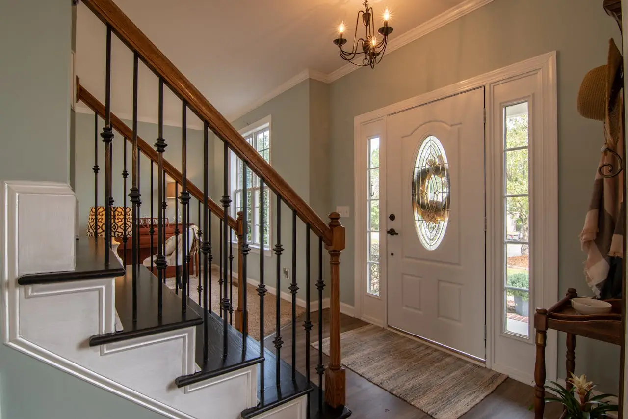 hero-img-01 Inviting modern hallway with staircase, chandelier, and natural daylight.