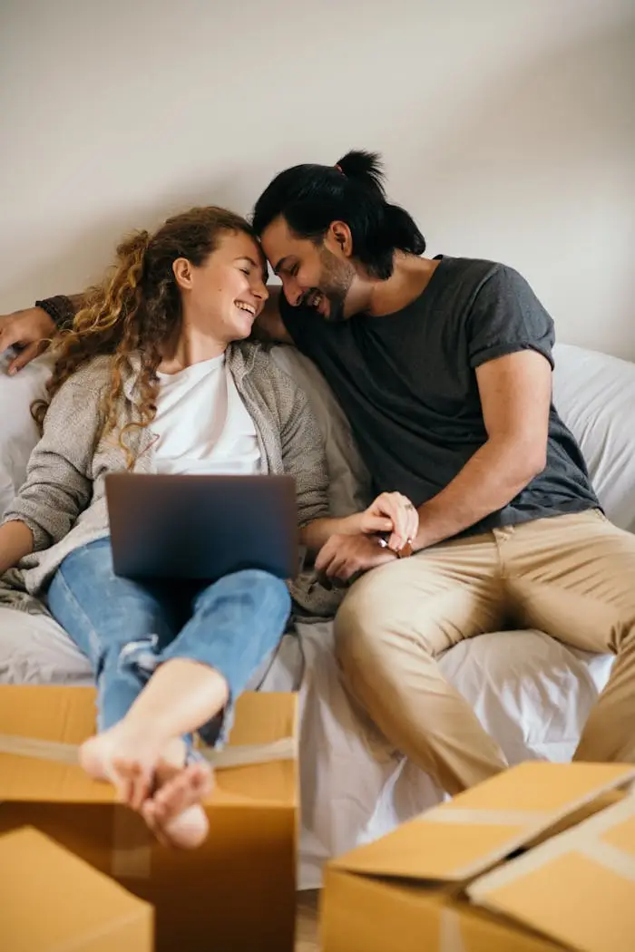 Laughing couple relaxing with a laptop among moving boxes in their new home. A fresh start together.